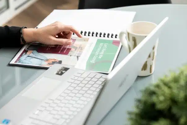 a spiral-bound notebook beside an open laptop