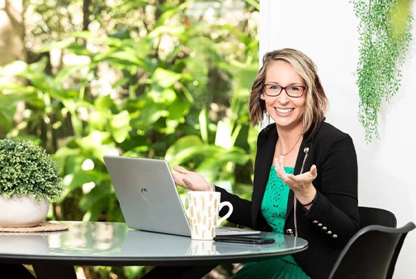 smiles while sitting at a table with a laptop and mug