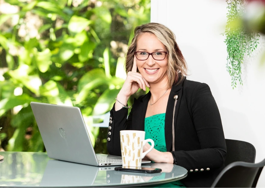 sits at a glass table with a laptop and a mug sits at a glass table with a laptop and a mug